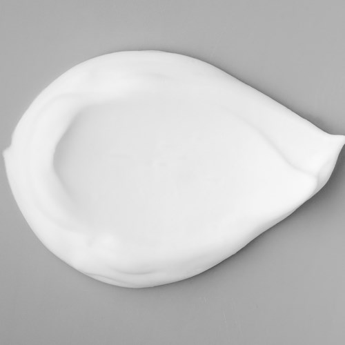Weiße Creme oder Lotion in Tropfenform auf grauem Hintergrund.