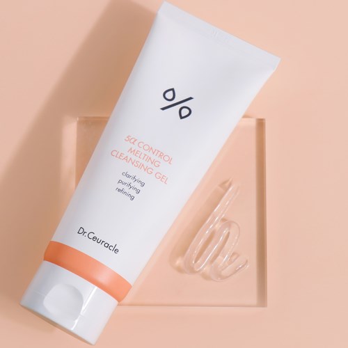 Eine weiße Tube mit der Bezeichnung '5% control melting cleansing gel' und etwas Gel daneben. Die Tube liegt auf einem hellrosa Hintergrund.