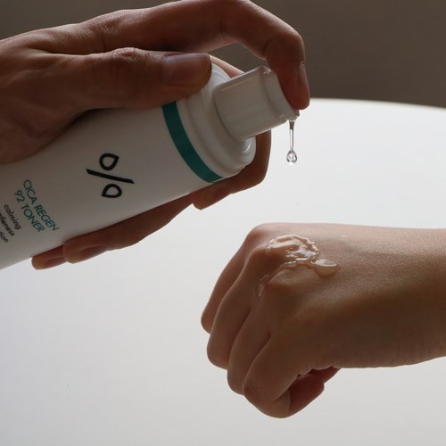En person påfører lotion eller krem på hånden, med en dråpe som faller fra flasken til huden.