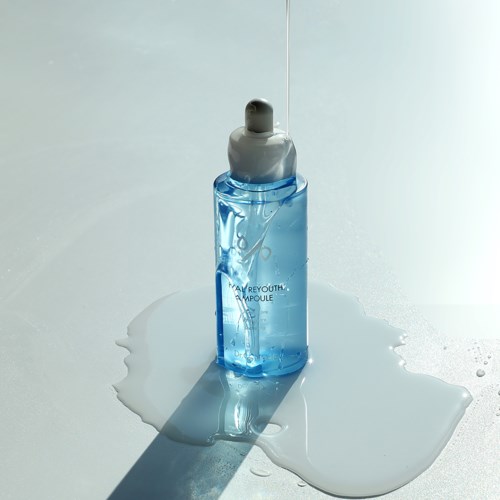 Eine blaue Hautpflegeflasche mit Tropfenzug, die etwas Flüssigkeit auf eine weiße Oberfläche tropft.