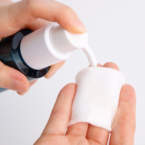 En person applicerar lotion eller kräm på en bomullspad som hålls i handen.