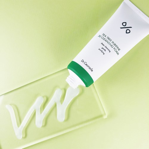 A tube of foam with green and white packaging, labeled 'Tea Tree Purifying & Cleansing Foam,' next to a green background.