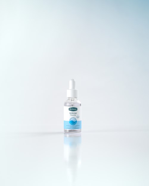 En lille gennemsigtig flaske med dråbetænger, mærket som serum, står alene på en simpel hvid overflade.