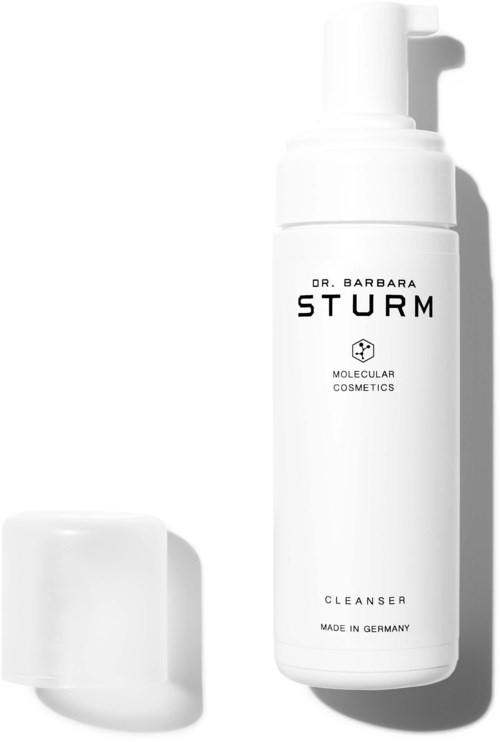 En vit flaska med Dr. Barbara Sturm hudvårdsprodukt med pump och en liten vit behållare i närheten.