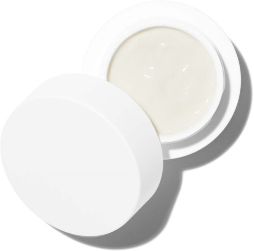 En liten, rund, vit behållare öppen, visar kräm eller lotion inuti med ett lock i närheten.