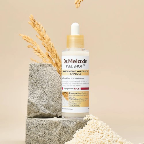 Een huidverzorgingsfles met label Dr. Melaxin Peel Shot staat op stenen met gedroogd graan en witte rijst eromheen.