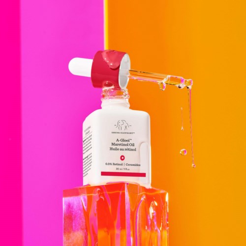 En flaska med hudvårdsolja med droppare, placerad på en färgglad rosa och orange bakgrund.