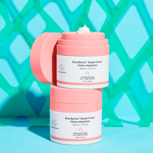 Two pink containers of Bora Barrier Repair Cream stacked against a bright blue background with a green pattern.