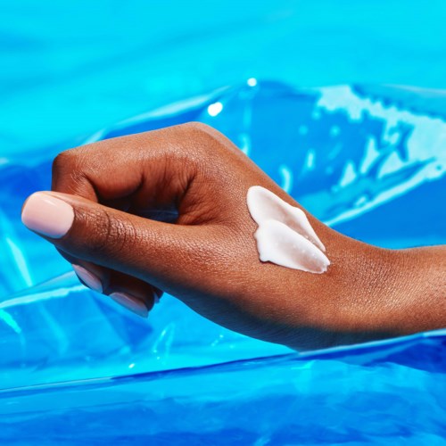 En hand med lotion på huden, nära en pool, blått vattengrad bakgrund.
