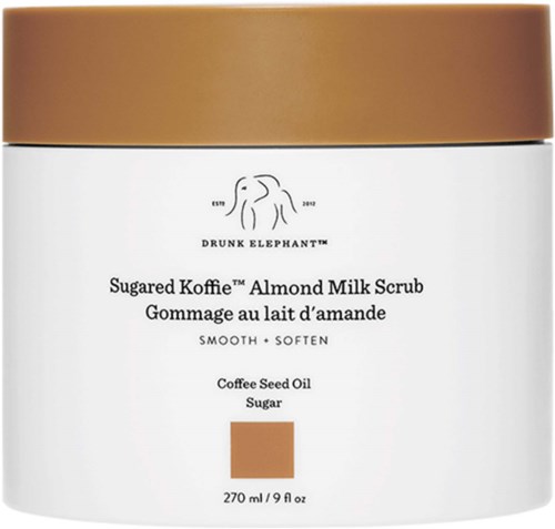 En vit burk med guldkant som innehåller Mandelmjölkskrubb, med ingredienser som kaffebärsolja och socker, lovar slät hud.