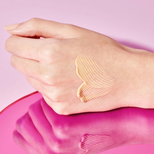 A hand with painted stripes on the back, resting on a pink surface, against a pink background.