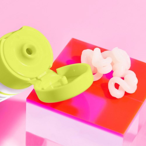 En limegrön flaska med vita tops och bomullspinnar på en rosa och röd kub, bakgrund rosa.