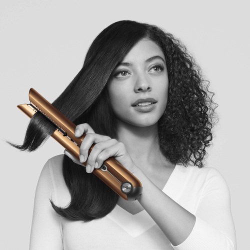 A woman with straight and curly hair is styling her hair with a hair straightener. She appears focused.