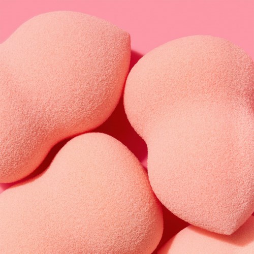 Tre rosa makeupsvamper med rundt form på en rosa bakgrunn.