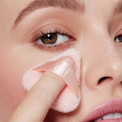 A person removes makeup from their face using a soft cloth, focusing on the cheek area.