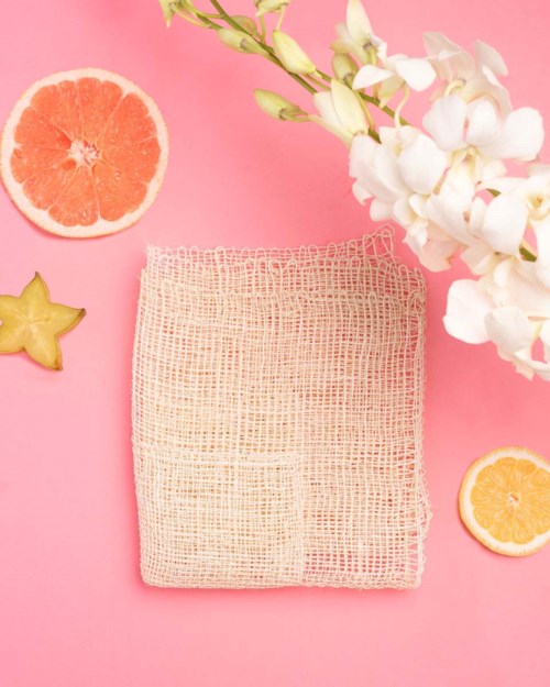 En rosa bakgrund med vita blommor, två citruskivor, en stjärnfärgad frukt och ett beige nätkläde.