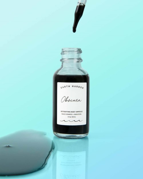 Een kleine fles met pipet, gelabeld Earth Harbor, met een donker water. Een plas van de vloeistof ligt op het oppervlak.