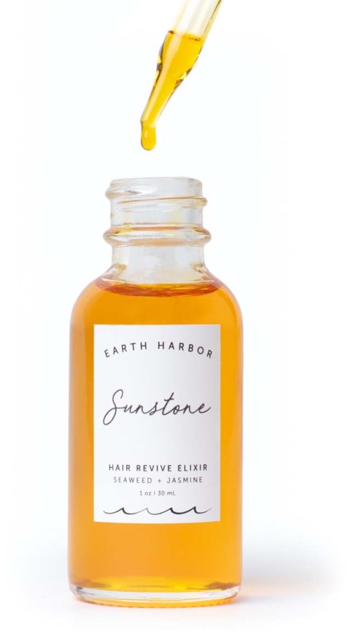 En liten tratt droppar gul vätska i en flaska märkt 'Sunstone Hair Revive Elixir' med tång och jasmin ingredienser.