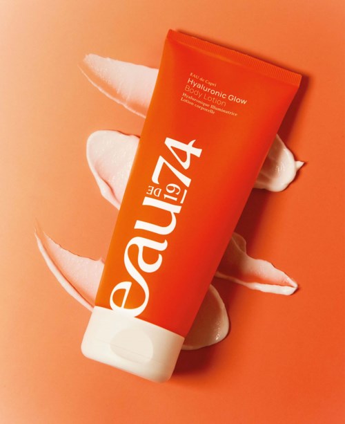 Orange tube of body lotion labeled 'Hyaluronic Glow' with white cream around it.