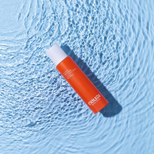 A red bottle of sunscreen floats on clear blue water. Sunlight makes ripples and shadows on the water surface.