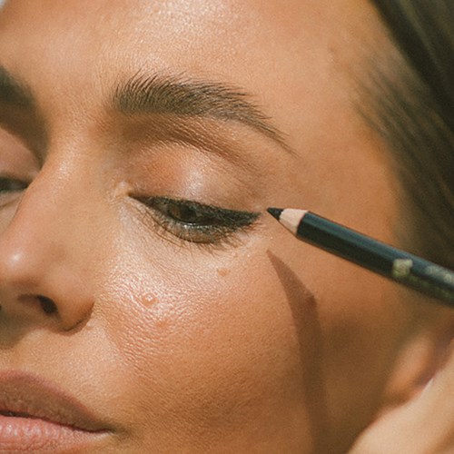 Eine Person trägt Eyeliner mit einem kleinen Pinsel auf das Augenlid auf.