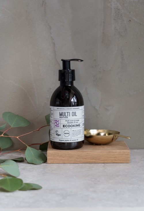 A dark brown bottle labeled 'Multi Oil' with a pump, placed on a wooden board with green leaves nearby.