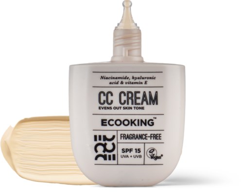 En hvid flaske med CC-creme med spids, ved siden af en klat af cremen. Den har SPF 15 og er parfymefri.