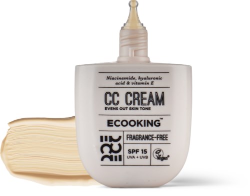 En hvid flaske med ansigtscreme med dyse, mærket med ingredienser og SPF 15, ved siden af en stak creme.