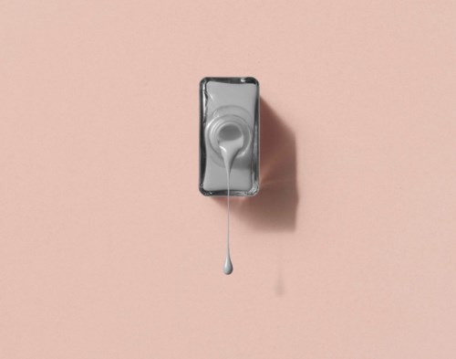 A grey bottle with liquid spilling out, placed on a pink background, casting a shadow.