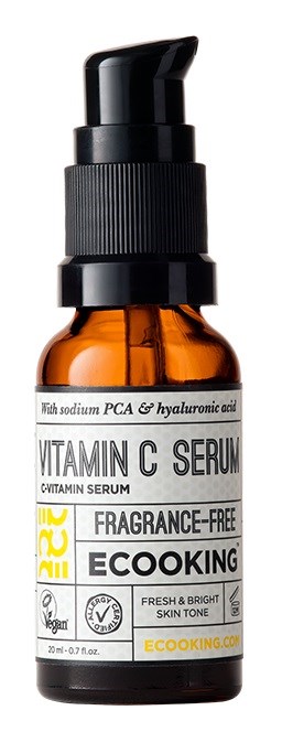 A small amber bottle with a black pump dispenser, labeled 'Vitamin C Serum' and 'Fragrance-Free.'