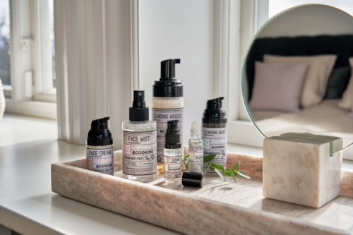 Skincare bottles and a mirror on a marble tray in a bright, cozy bedroom setting.