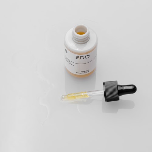 Een kleine fles met 'EDO' label en een druppelaar met oranje vloeistof. Fles ligt open op een witte ondergrond.