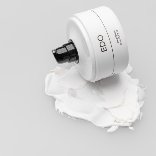 Een witte tube met een zwarte uitloop, gemerkt 'EDO', lekt crème of lotion op een grijze ondergrond.