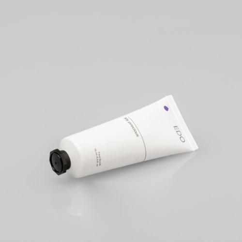 Een witte tube huidverzorgingsproduct met zwarte dop, ligt op een grijze ondergrond.