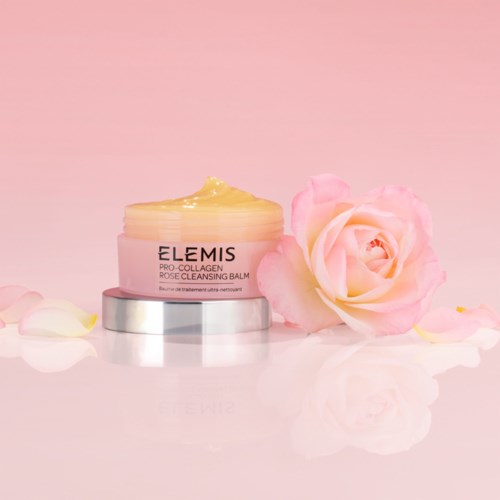 A jar of pink cream with a pink rose, on a reflective surface with rose petals around.
