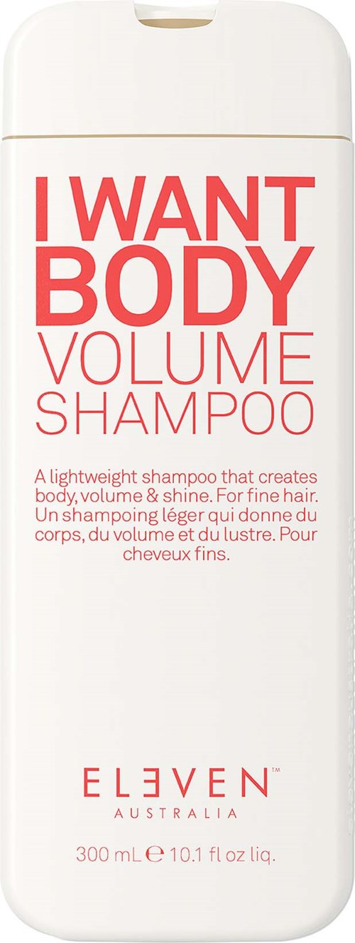 En vit flaska med röd och rosa text som annonserar I WANT BODY VOLUME SHAMPOO av ELEVEN, Australien.