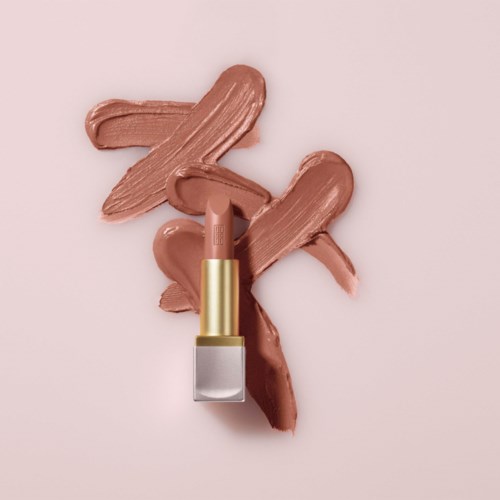 En leppestift med fire prikker av beige leppestift smurt på en rosa bakgrunn.