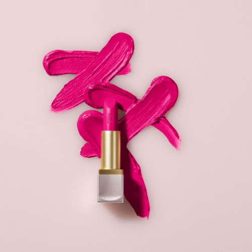 Leppestift med rosa strøk og smus på lys rosa bakgrunn.