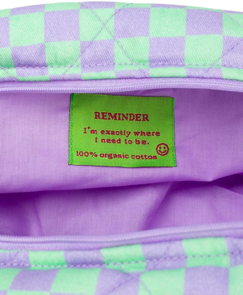 A fabric label inside a purple bag says it's made of 100% organic cotton and gives a reminder message.