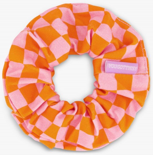 A colorful fabric hair scrunchie with pink and orange checkered pattern and a small label reading "YOU GOT THIS."