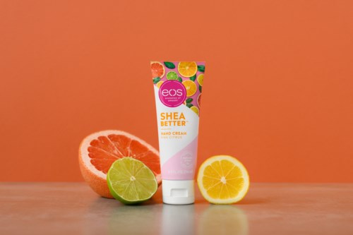 En handkrämstub står mellan grapefrukt, lime och citronskivor på en neutral yta och orange bakgrund.