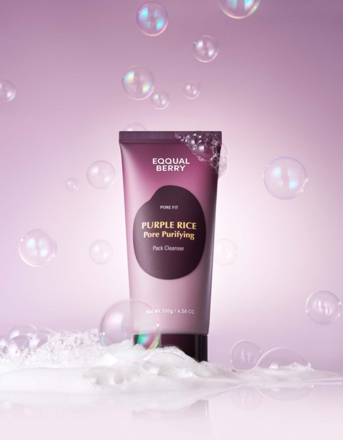 En tube med Purple Rice Pore Purifying Pack Cleanser omgitt av såpbobler mot en rosa bakgrunn.