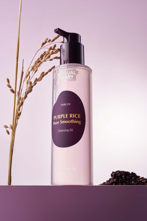 En klar flaske med rengjøringsolje merket 'Purple Rice Pure Smoothing' med tørkede riskorn og bønner rundt den.