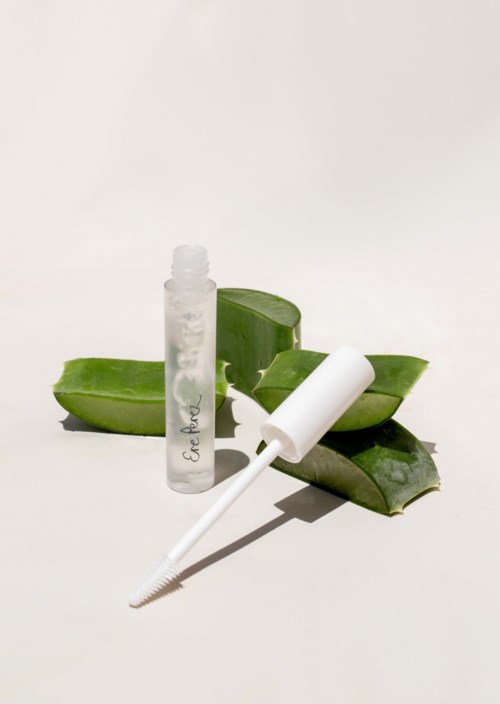 Selkeä pullo ja valkoinen tippa, taustalla aloe vera -lehdet. Asettelu on siisti ja yksinkertainen.