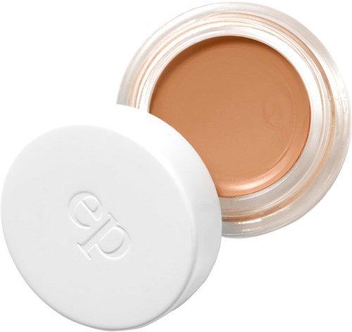 En beholder med beige creme eller foundation og en hvid låg med logo. Beholderen er åben og viser produktet inde i.