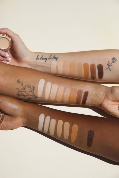 Tre arme med forskellige hudtoner viser makeupprøver og tatoveringer, herunder blomster, tekst og linjer.