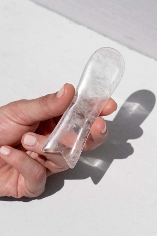 En hånd holder et gjennomsiktig, buet glassobjekt med en glatt overflate. Sollys skaper en skygge på en hvit overflate.