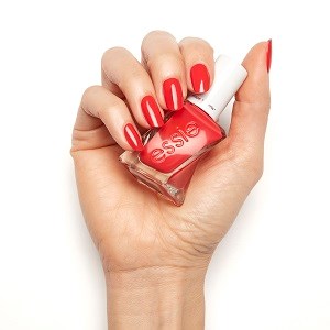 Eine Hand hält eine Nagellackflasche und trägt roten Nagellack auf. Die Nägel sind bereits rot.