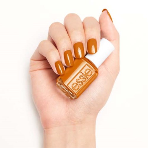 En hånd med neglene malt i lys oransje holder en flaske med Essie neglelakk.