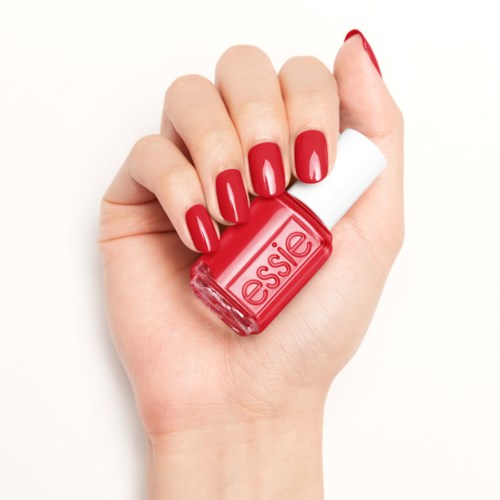 En hand med röda målade naglar håller en röd Essie nagellacksflaska.